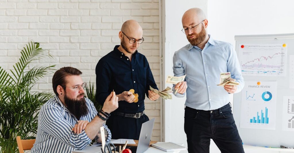 Três homens em ambiente de escritório analisando dinheiro e gráficos financeiros.